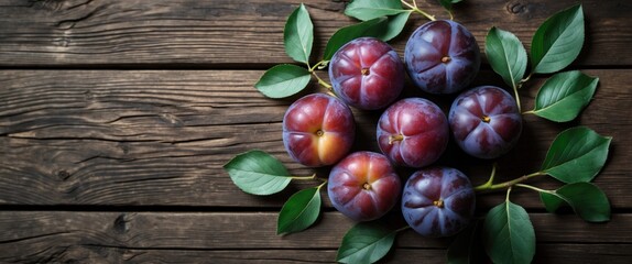 Fresh plums with leaves on rustic wooden table background, flat lay with copy space for text.
