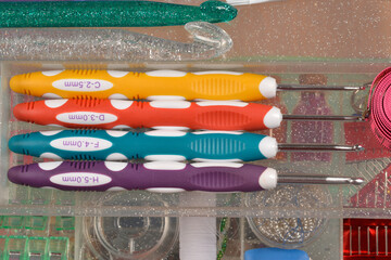 A colorful set of four ergonomic crochet hooks is neatly stored in a clear craft organizer,...