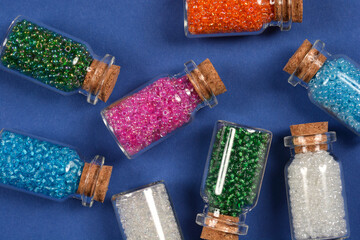 A collection of small glass bottles, each stoppered with a cork and filled with colorful seed...