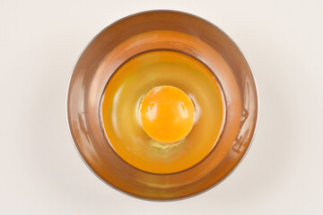 A single raw egg with a vibrant orange yolk is perfectly centered in a stainless steel bowl against...