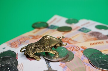 A bull figurine with coins and paper bills on a green background. Business and finance.