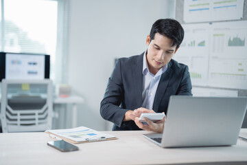 Young businessman calculating and working with laptop and documents on desk in modern office,...