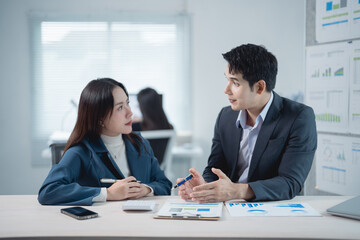 Two asian business partners are discussing financial charts and graphs while sitting at office...