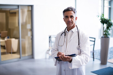 Doctor with stethoscope is writing notes on clipboard near glass partition and beige chairs