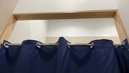 Changing room. Close-up photo of blue fabric curtain hanging on a shiny metal rod with round wall mounts