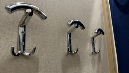 Close-up photo of three chrome coat hooks mounted on textured beige wall
