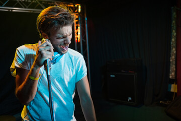 Male singer holding mic stand and singing passionately on stage with blue headphones, metal truss