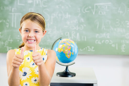Globe resting on white desk near chalkboard showing math and science formulas in classroom