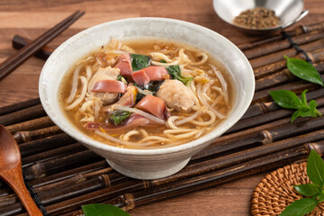 Taiwanese squid thick noodle soup in ceramic bowl on wooden table background.