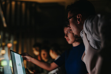 A diverse group of business people collaborate on a project, analyzing data on a computer screen during a late-night work session, striving to meet deadlines and generate innovative solutions.