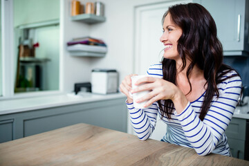 White ceramic mug resting on light wood kitchen table near toaster and open shelf with jars
