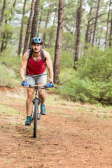 Male cyclist riding mountain bike with helmet and hydration pack along dirt trail in pine forest