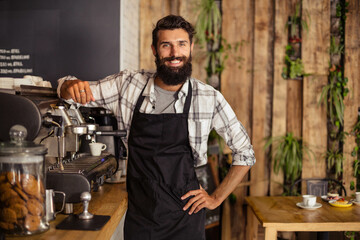 Male barista in black apron leaning on wooden counter at cafe preparing espresso with cookie jar