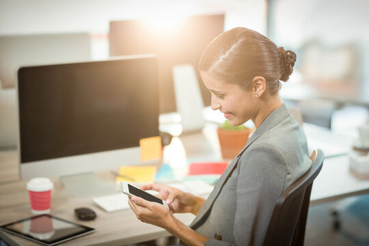 smartphone sitting beside monitor on sunlit office desk with red coffee cup and sticky notes