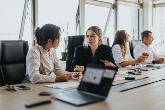 A multicultural group of business people engaged in a serious meeting around a conference table. Focused individuals are discussing strategies and ideas in a modern, well-lit office environment.