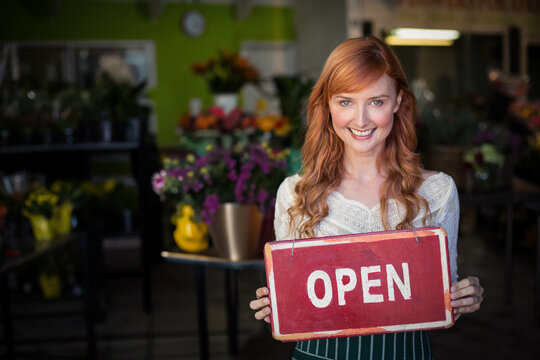 Red OPEN sign displaying near entrance of flower shop, surrounded by colorful bouquets and plants