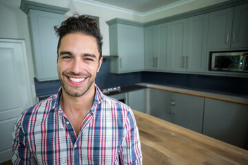 Smiling man standing in kitchen beside wooden island, cabinets and dark backsplash, copy space
