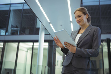 Fototapeta premium Businesswoman wearing suit standing at glass railing in lobby holding white tablet, copy space