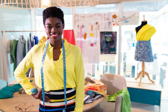 African American woman wearing yellow blouse examining fabrics with measuring tape in design studio - Powered by Adobe