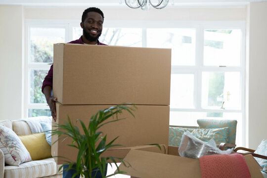 Smiling African American man carrying cardboard boxes in living room with bubble wrap