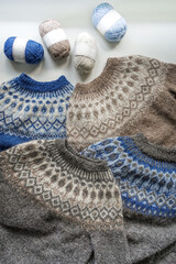 Nordic pattern blue and brown knitted wool sweaters lied down on each other with ball of yarn on top with white background