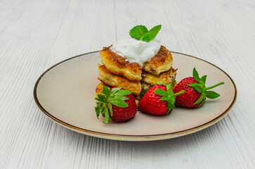 Cottage cheese pancakes (syrniki) with fresh strawberries and sour cream.