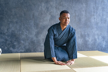 A black man wearing a yukata sitting on a tatami mat