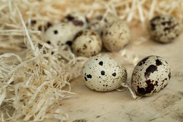 close up of quail eggs scattered on a wood surrounded by straw