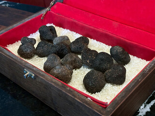 A collection of dark truffle rests in a luxurious wooden box lined with rice, showcasing their unique shape and rich texture at a gourmet market