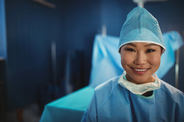 Asian female surgeon standing right of draped table in operating room wearing scrub cap, copy space