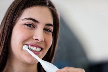 Woman brushing teeth with white electric toothbrush in bathroom near mirror wearing light top © WavebreakMediaMicro