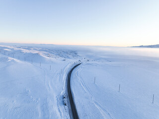 An aerial view of a seemingly endless road extending through an expansive, snow-covered plain under...