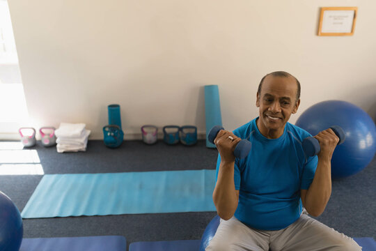 Fototapeta Blue dumbbells performing bicep curls while balancing on exercise ball near kettlebell row in gym