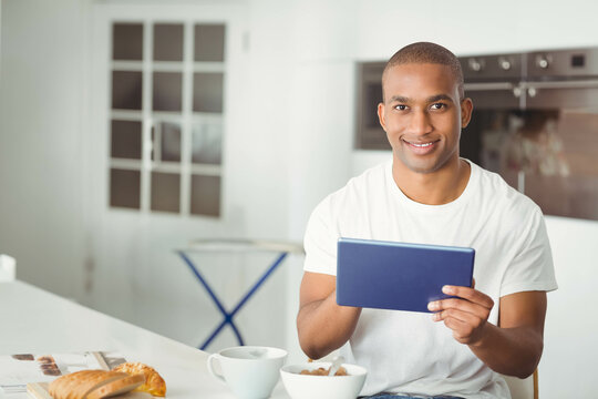 African American man using tablet at kitchen counter with croissant and cereal bowl, copy space