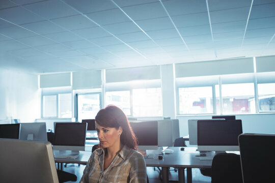 Mid-adult woman typing on keyboard at open-plan office desk, focusing on large monitor, copy space