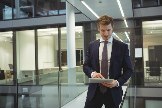 Male business professional standing on glass walkway at office level checking tablet, copy space