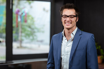 Fototapeta premium Man standing in office by glass window with ribbons wearing glasses and suit jacket, copy space