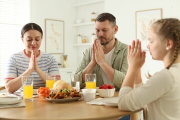 Family praying together before dinner at table indoors