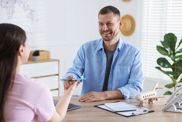 Obraz premium Travel agent giving passport with ticket to woman at wooden table in office