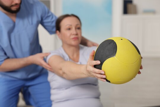 Doctor and patient exercising with medicine ball in clinic, selective focus
