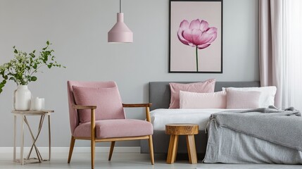 Pink armchair and wooden stool in bedroom with poster above grey bed (Real photo)