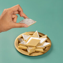 Hand Picking up Indian Kaju Katli Mithai from a Brass Plate Stacked up Together