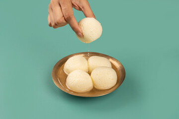 Traditional Indian Rasgulla Mithai in a Brass bowl being picked up by a hand to eat