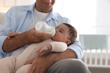 Obraz premium Father feeding his little baby with bottle on armchair at home, closeup