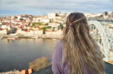 A young woman with long, flowing hair admires the breathtaking view of Porto by the serene riverbank