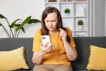 Woman with vision problem using smartphone on sofa at home