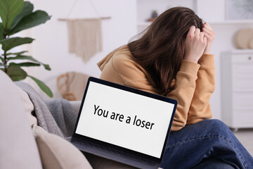 Cyber bullying. Upset teenage girl and laptop with text You Loser on sofa at home