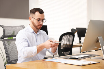 Man taking photo of document using scanning app on smartphone at desk in office