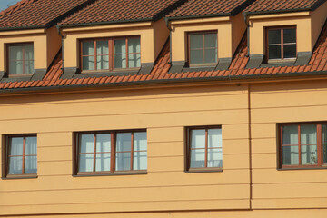 There is a yellow building that features a striking red tiled roof and has many windows throughout its structure, enhancing its beauty
