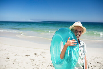 Naklejka premium Turquoise inflatable ring and straw sun hat resting on white sand by gentle turquoise sea waves